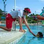 A lifeguard wearing the Red Cross Hip Fanny Pack helping a child get out of the pool.