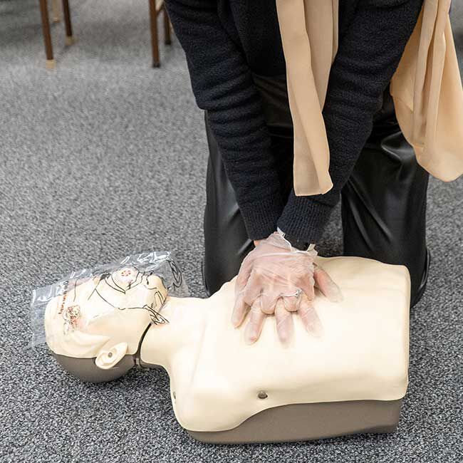 Student wearing clear gloves practicing chest compressions on a CPR manikin with a face shield.