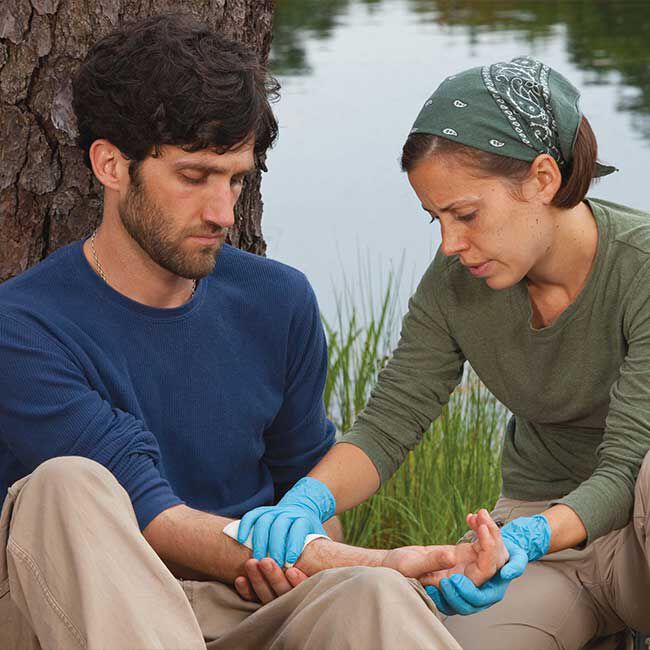 A person wearing blue nitrile gloves applying a bandage to an injured person.