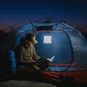 The LuminAID Max QI Lantern illuminated and hung up in a camping tent with a person reading a manual.