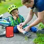 A parent applying a bandage from a Red Cross first aid kit to a child's shin.