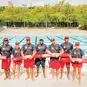 A group of lifeguards standing in front of a swimming pool holding rescue tubes.