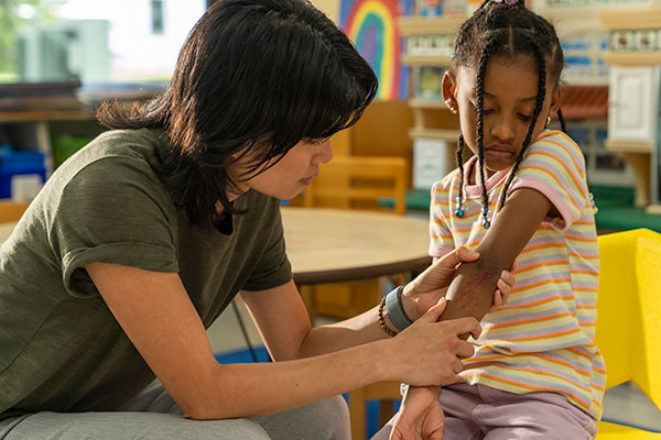 A Cincinnati, Ohio teacher inspects a scrape on a student's arm.