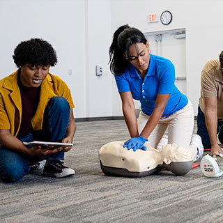 Red Cross Instructor teaching students in a CPR course to perform CPR on a manikin with a CPR mask.