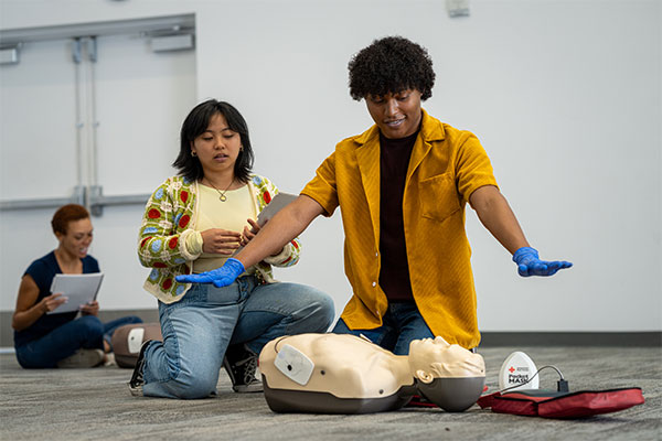 A student practices using an AED on a manikin in Tampa, Florida demonstrating the clear step with arms spread.