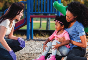 A nanny helping an injured child on the playground with first aid.